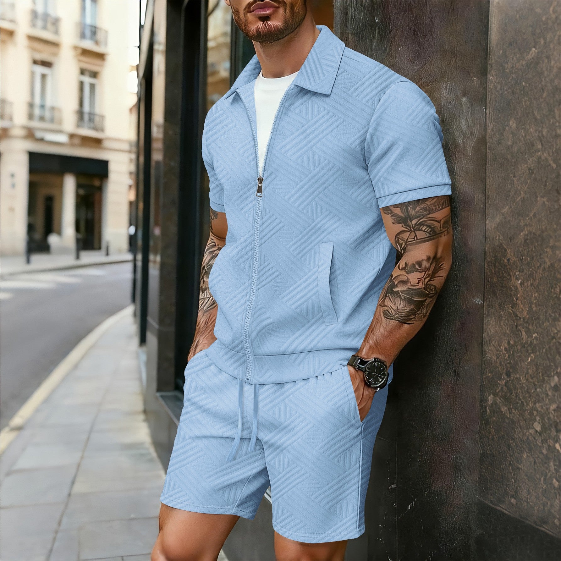 Man wearing a light blue textured outfit leaning against a wall on a city street.