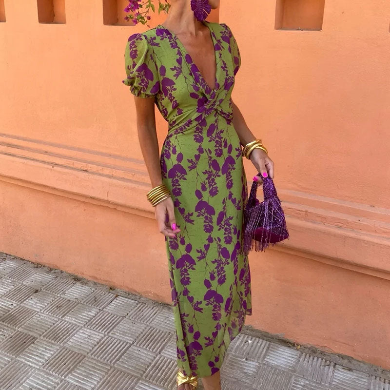 Woman in a green and purple floral dress standing against an orange wall.