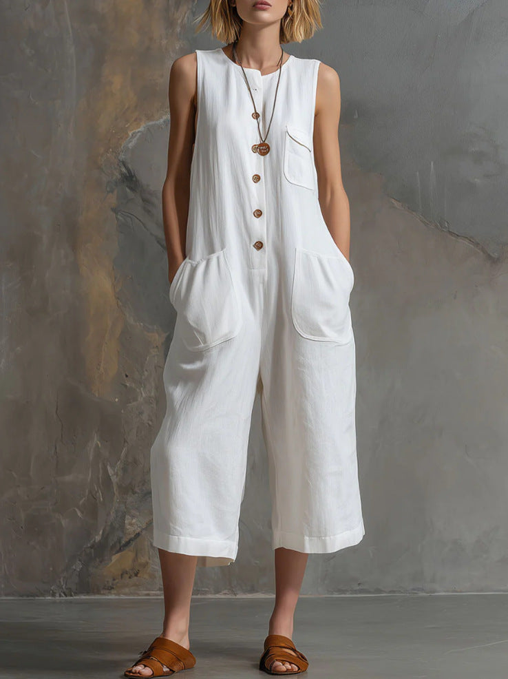 Woman wearing a white sleeveless jumpsuit with brown sandals against a gray background