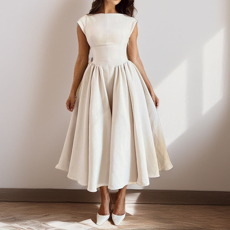 Woman wearing a white dress standing against a plain wall.