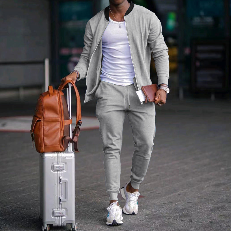 Person in gray outfit with suitcase and brown backpack walking on a street.