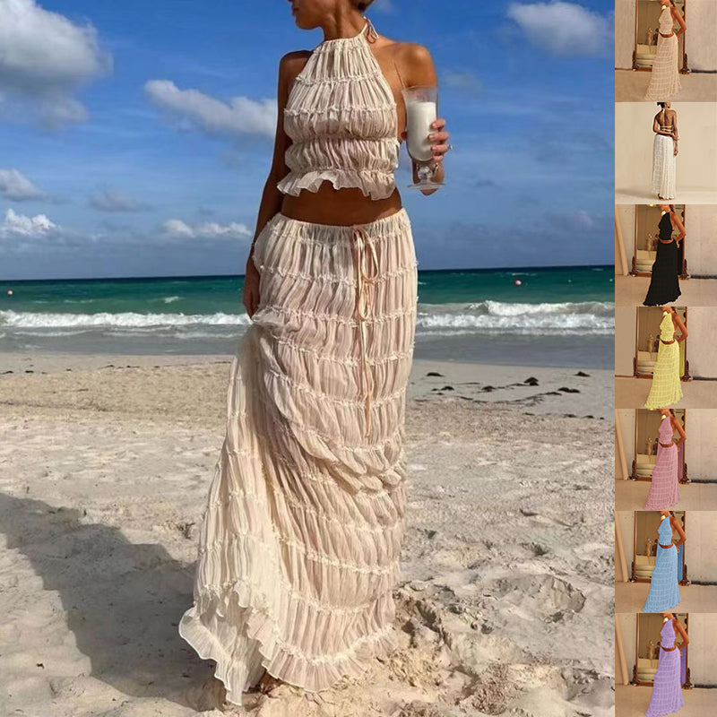 Woman in a long, light-colored dress standing on a beach with ocean view.