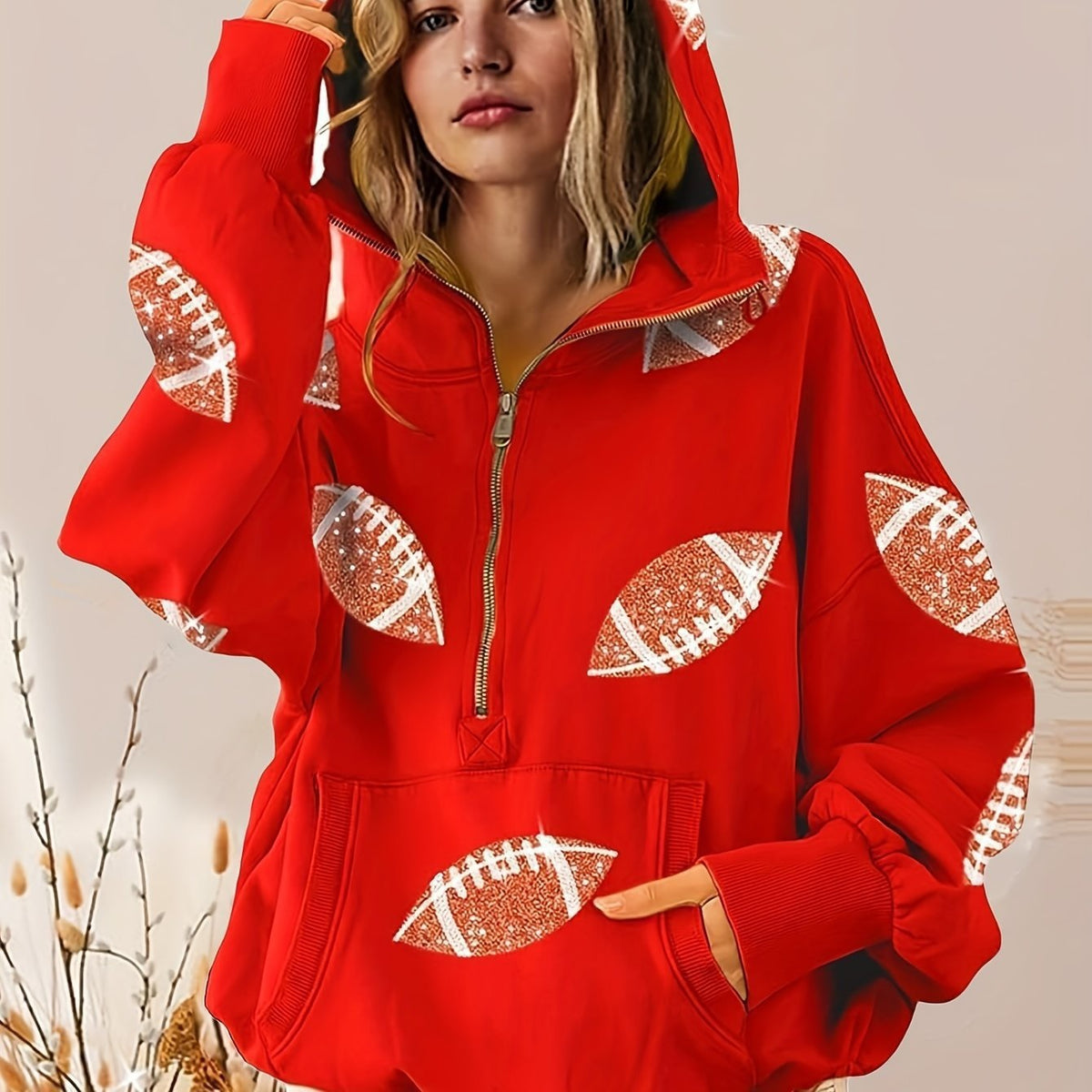 Red hoodie with football patterns worn by a person, against a neutral background
