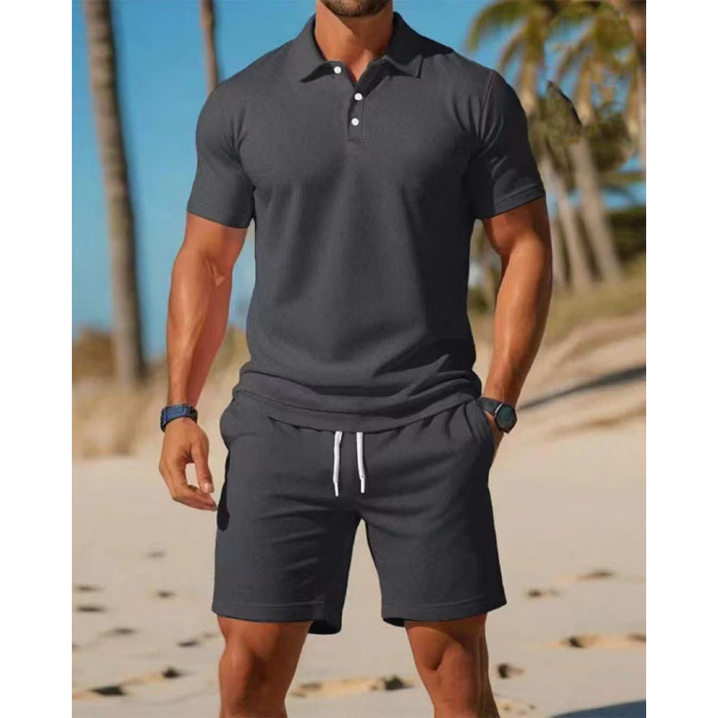 Man wearing a dark gray polo shirt and shorts on a beach.