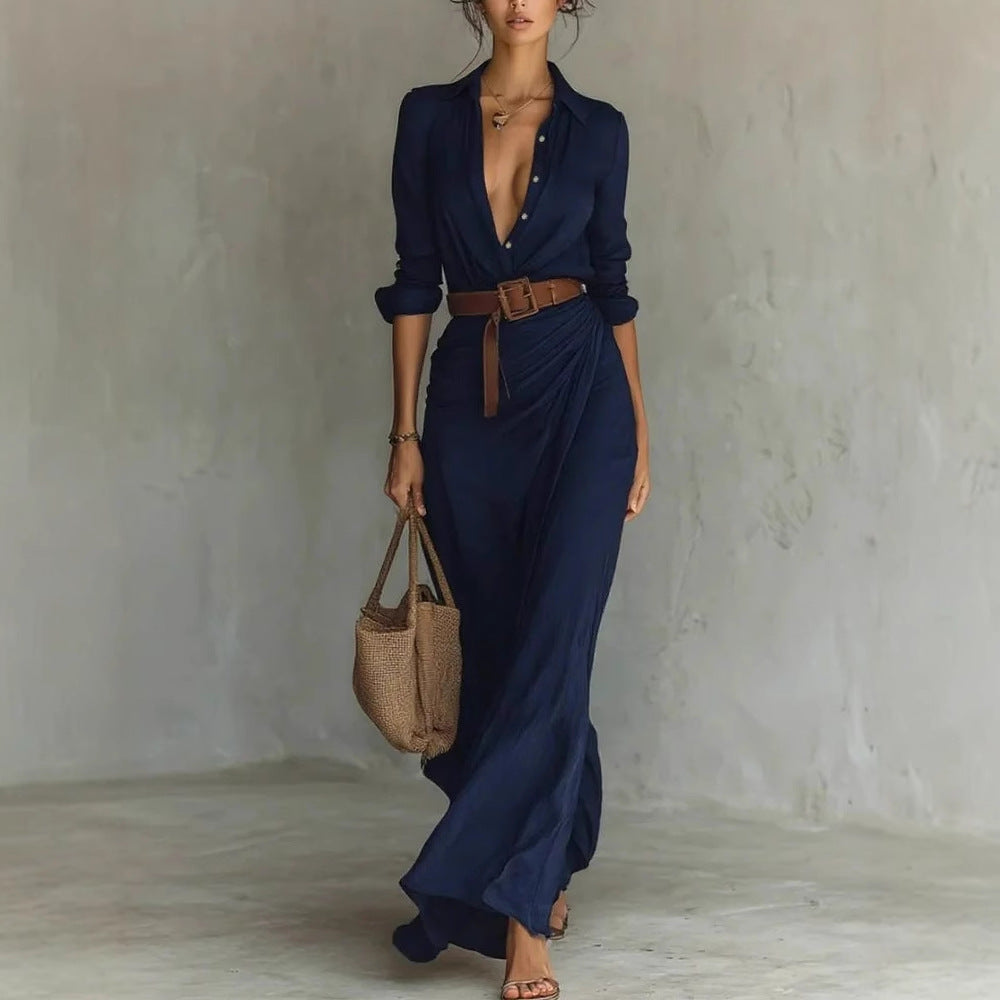 Woman in a long navy dress holding a brown bag against a plain background
