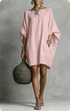 Woman wearing a pink dress holding a woven bag against a gray background