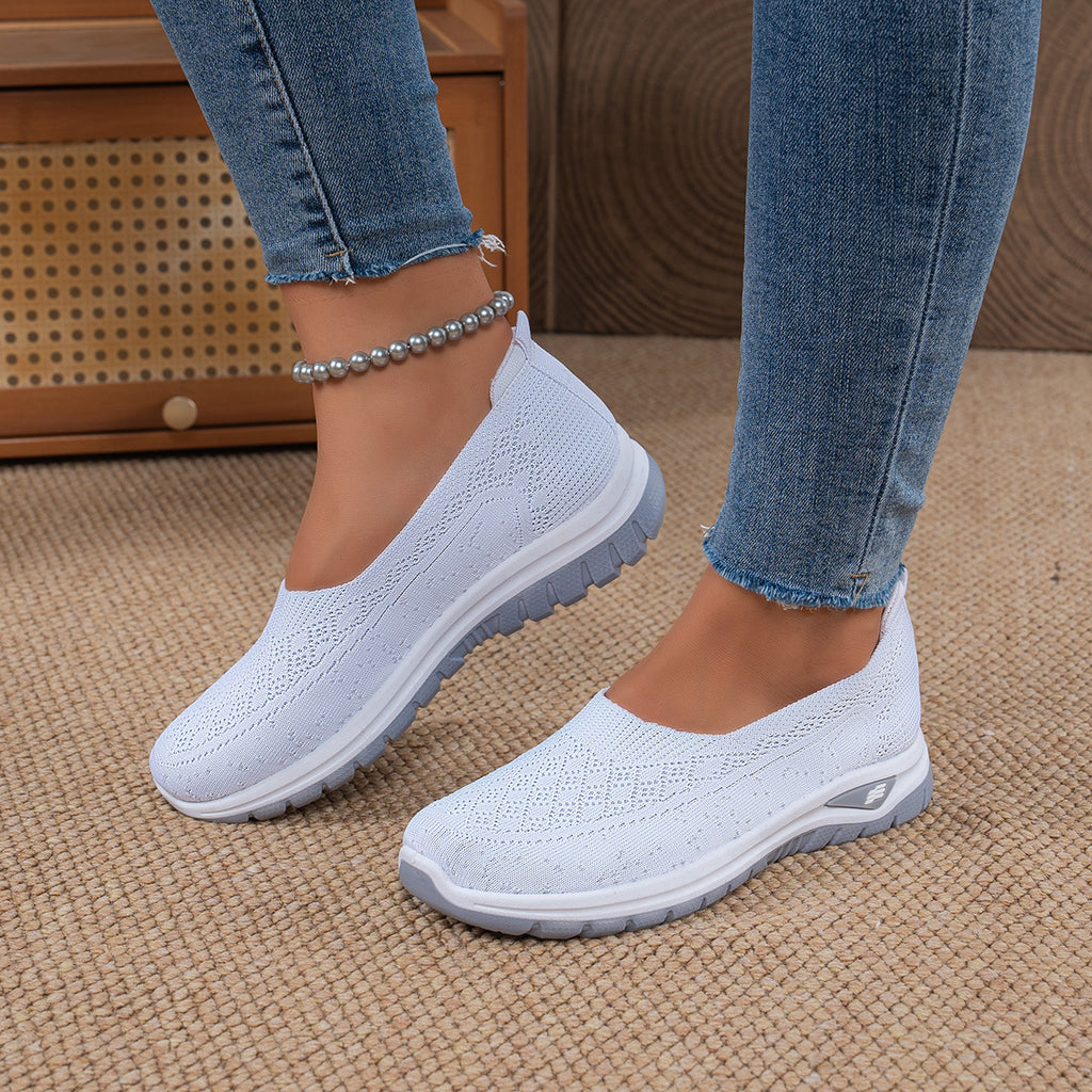 White slip-on shoes worn with blue jeans on a textured surface