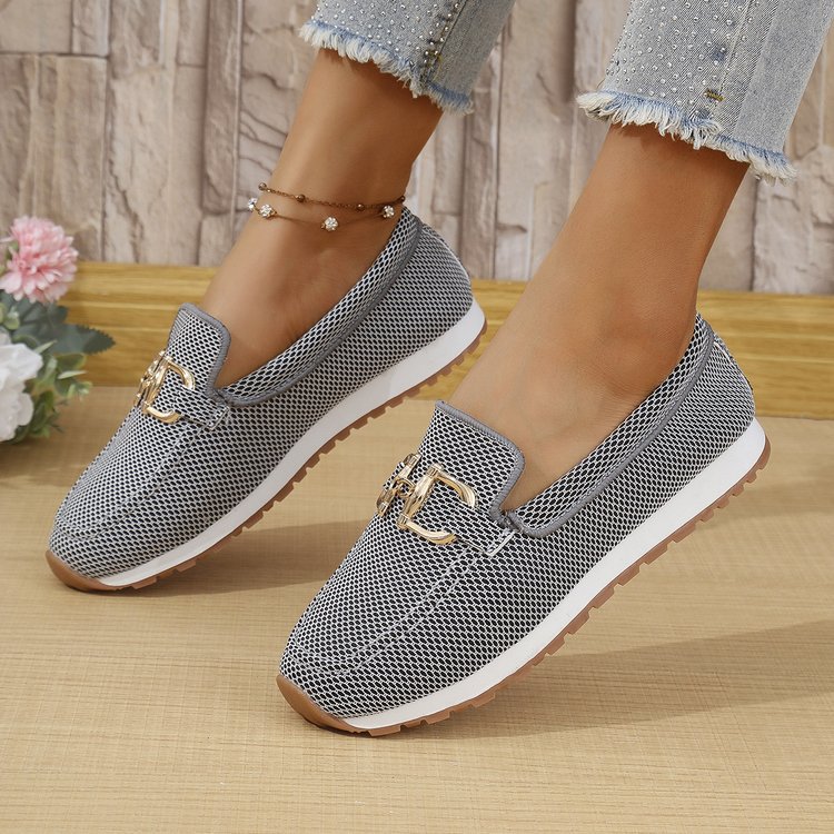 Gray mesh shoes with gold accents worn by a person on a wooden floor.