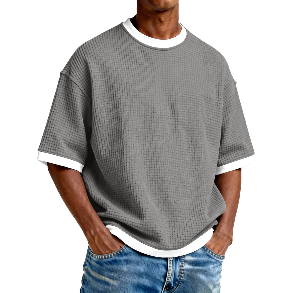 Man wearing a gray textured t-shirt with white trim and blue jeans on a white background