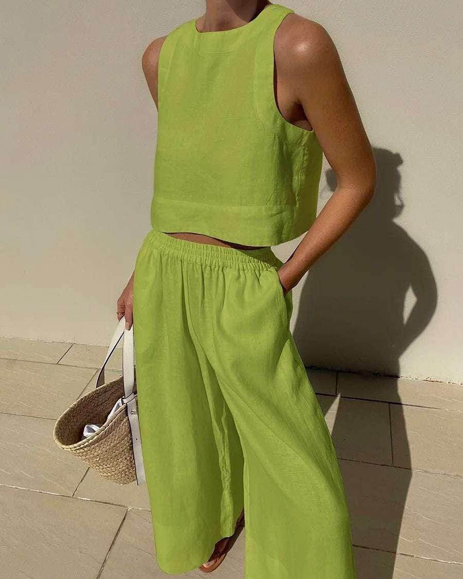 Woman wearing lime green sleeveless crop top and wide leg pants, holding straw tote bag