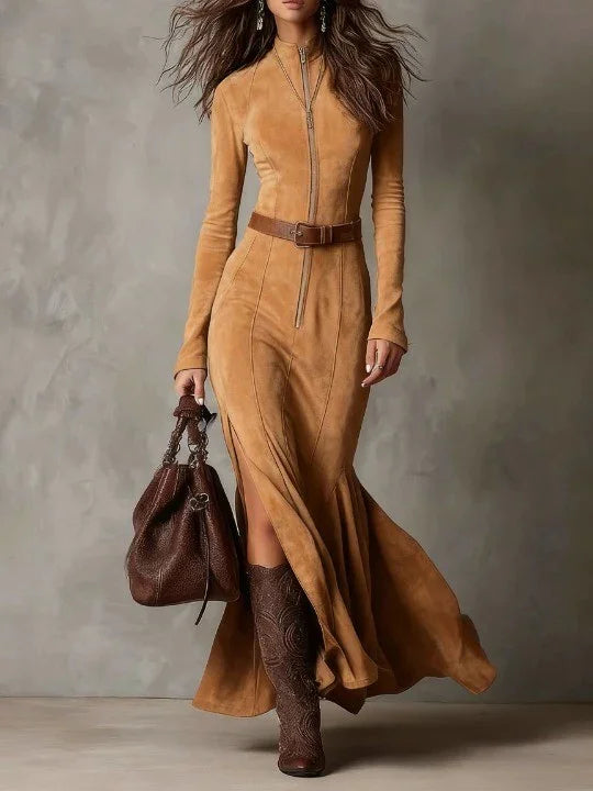 Woman wearing a long brown dress with a belt and holding a matching handbag against a neutral background