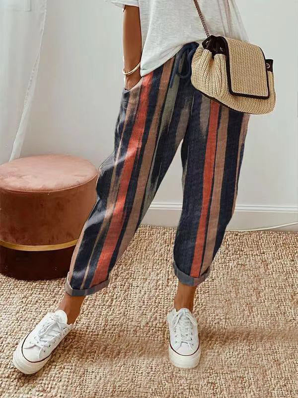 Person wearing striped pants and white sneakers with a straw bag indoors.