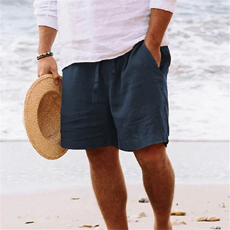 Person wearing navy shorts and holding a straw hat on a beach.