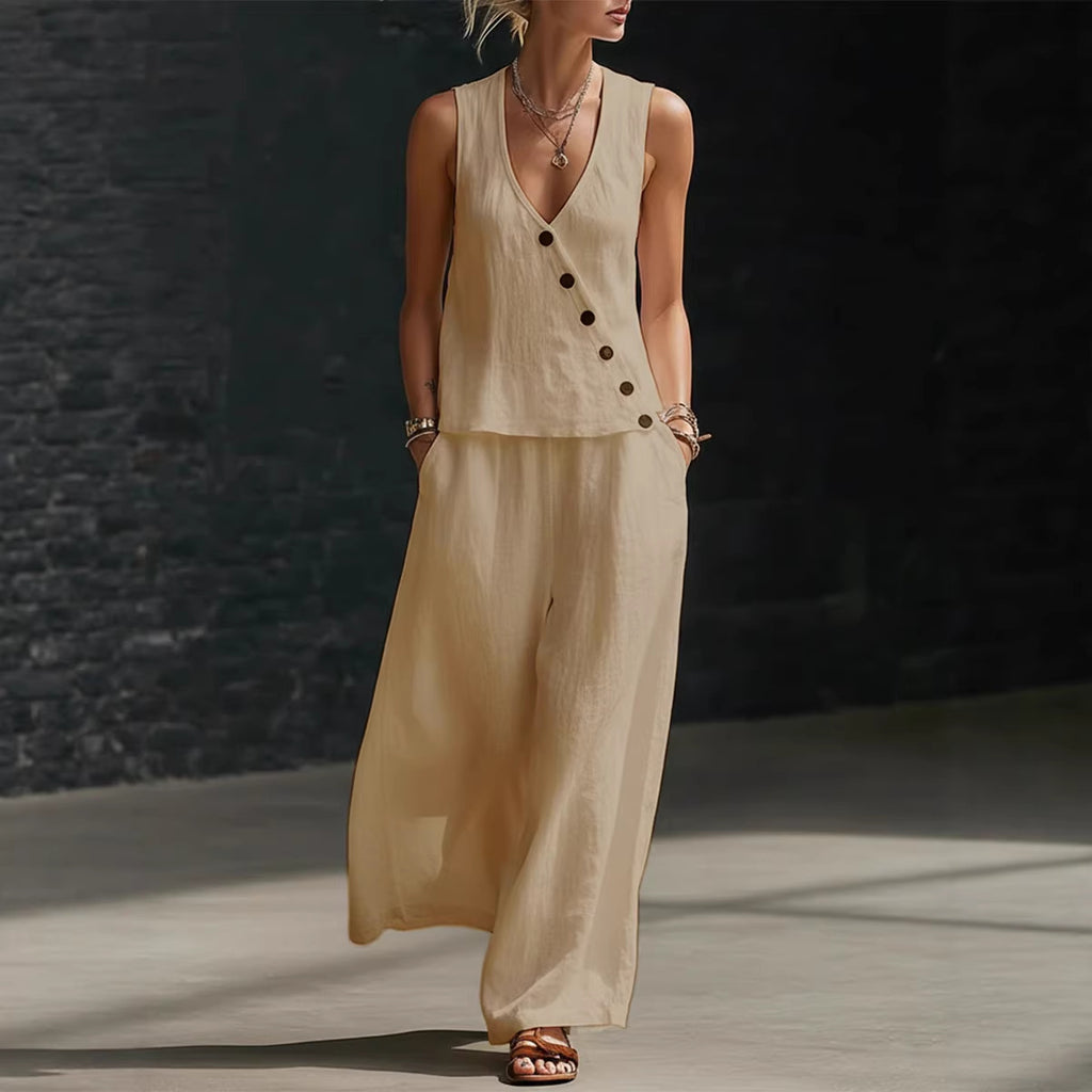 Woman wearing a beige sleeveless top and wide-leg pants against a dark brick wall.