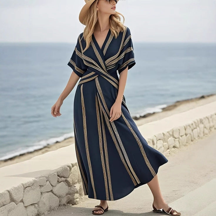 Woman in a navy dress with gold stripes walking on a beach.