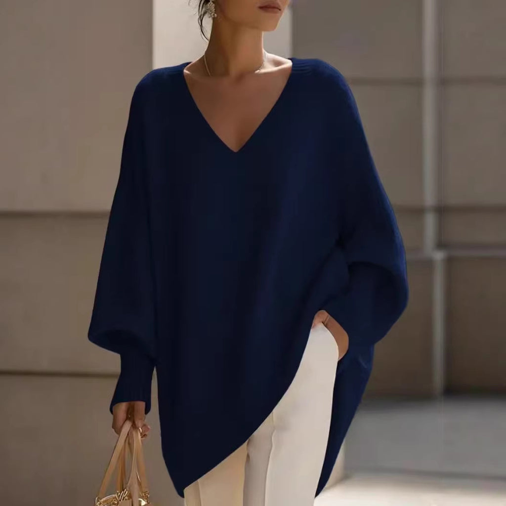 Woman wearing a navy blue poncho and white pants, holding a beige handbag.