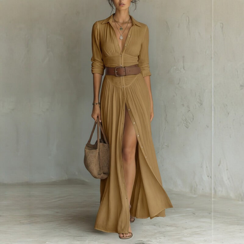 Woman wearing a long mustard yellow dress with a belt, holding a matching handbag against a plain background.