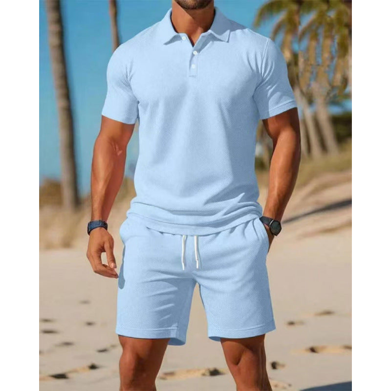Man wearing a light blue polo shirt and shorts on a beach.