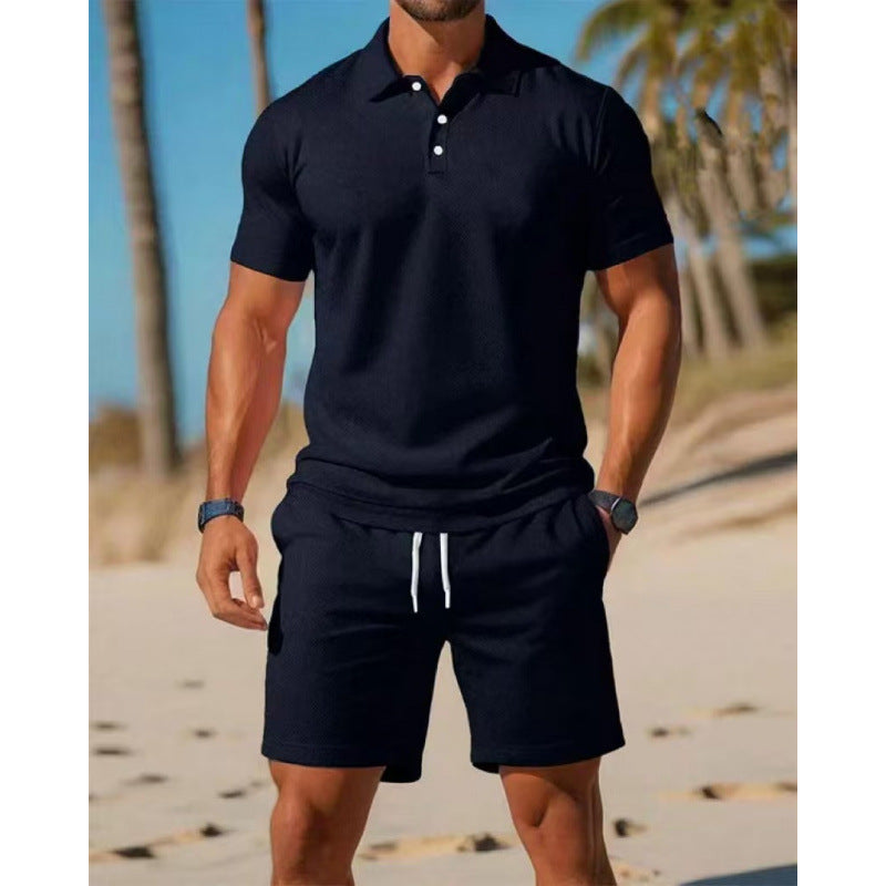 Man wearing a black polo shirt and shorts on a beach with palm trees in the background