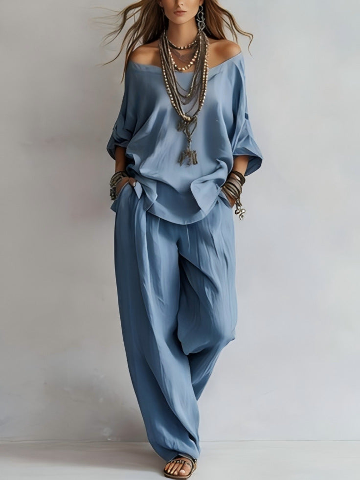 Person wearing a blue outfit with wide-leg pants and layered necklaces on a plain background