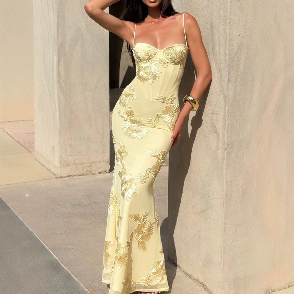Woman wearing a yellow evening gown with floral embroidery against a neutral wall.