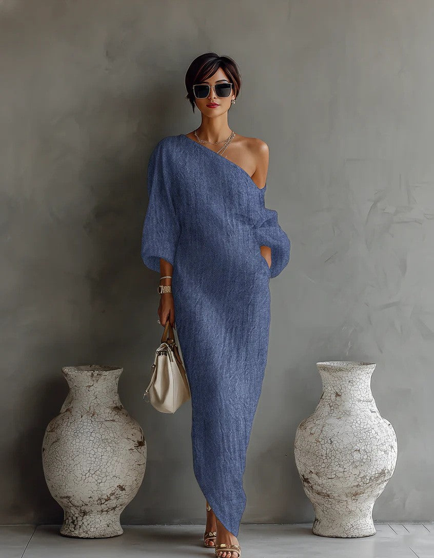Woman in a blue one-shoulder dress standing between two large vases against a gray wall.