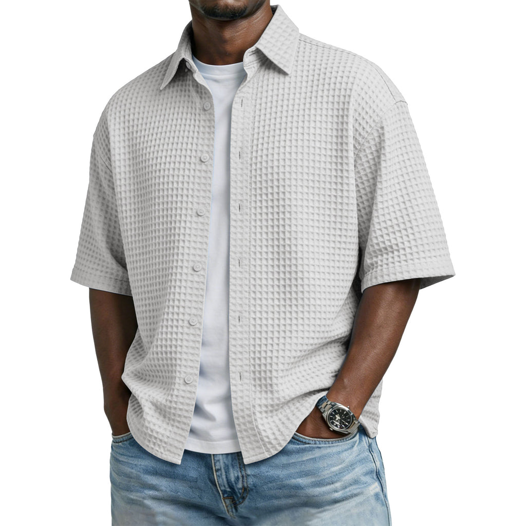 Man wearing a textured short-sleeve shirt over a white shirt with blue jeans on a white background