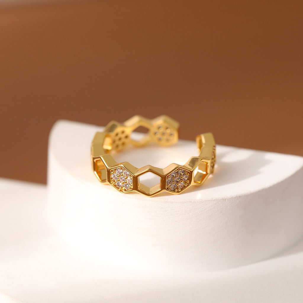 Gold ring with honeycomb design and embedded stones on a white surface with a brown background