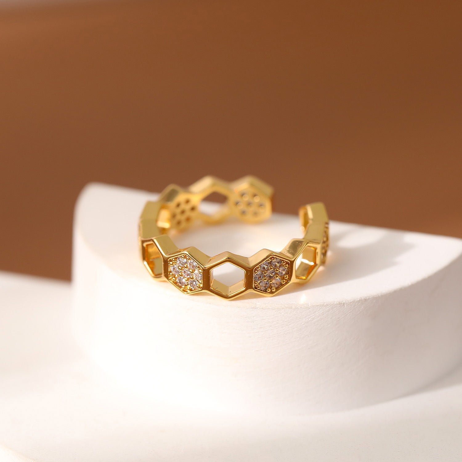 Gold ring with honeycomb design and embedded stones on a white surface with a brown background