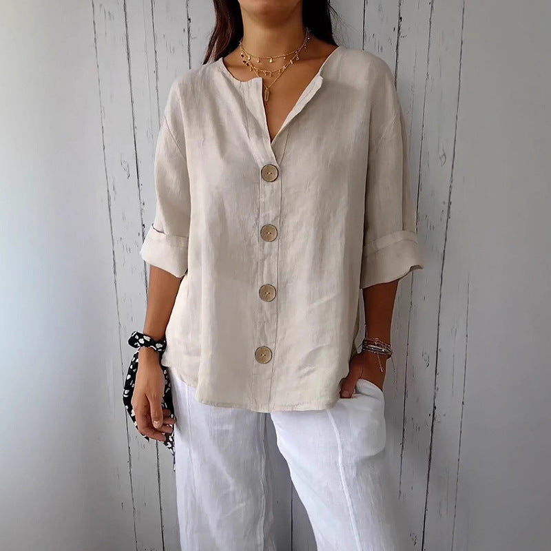 Person wearing a beige button-up shirt and white pants against a light wooden panel background