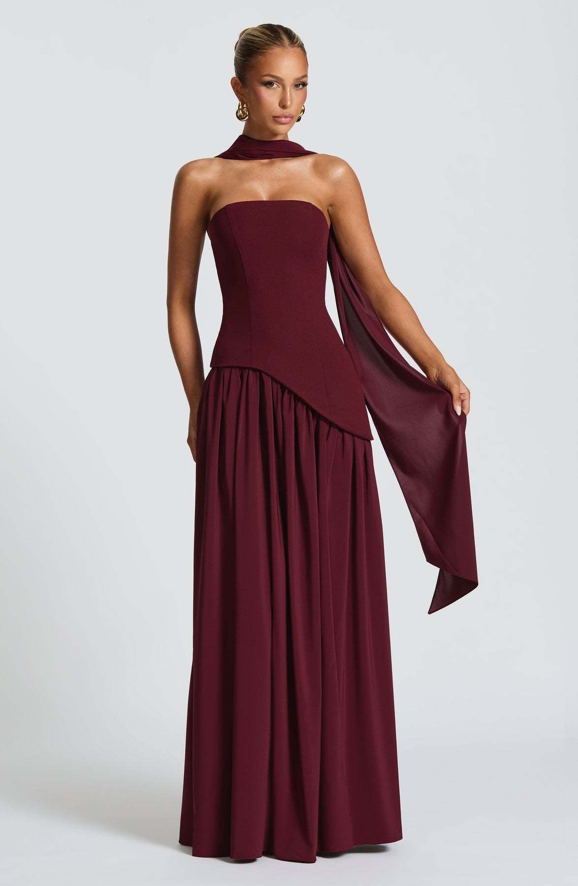 Woman wearing a burgundy halter neck gown with a draped effect on a white background