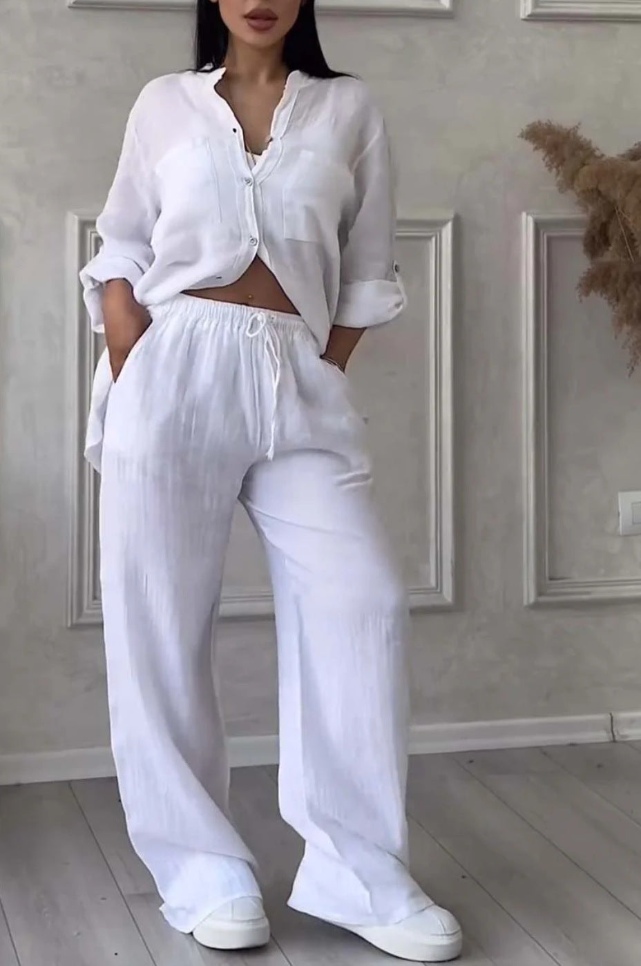 Person wearing a white outfit in a room with a neutral wall and wooden floor.