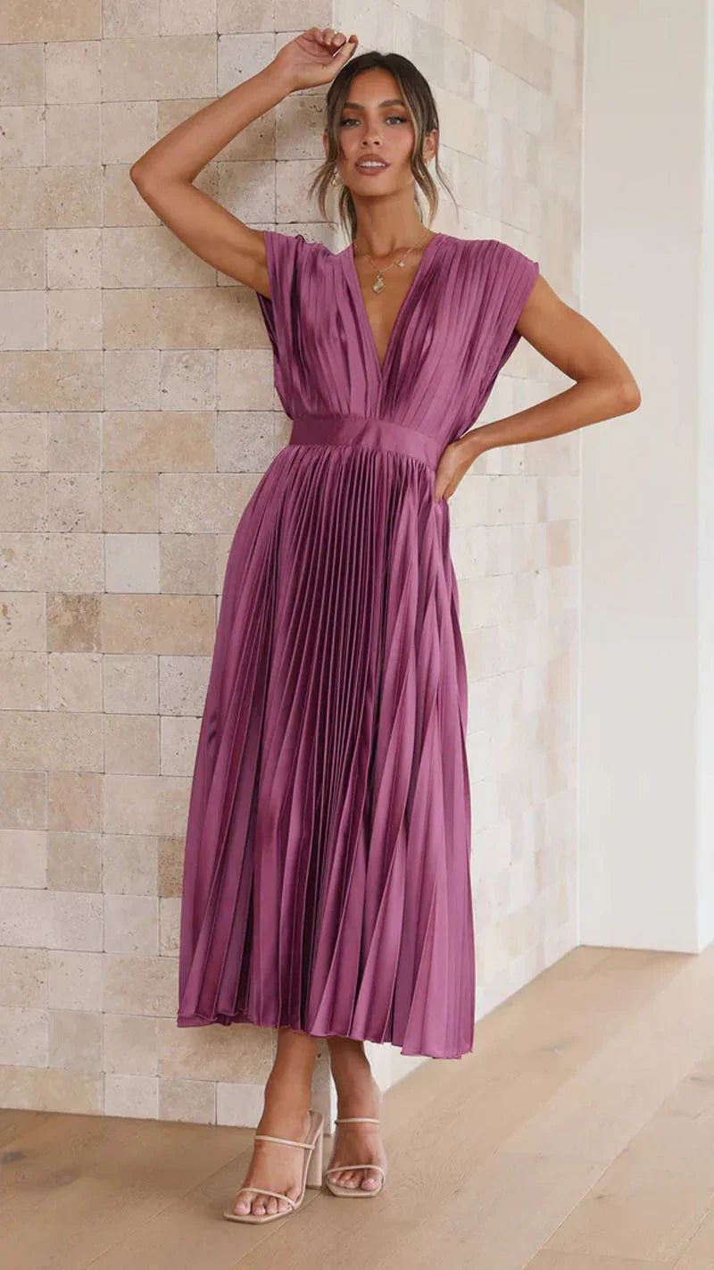 Woman wearing a purple pleated dress against a beige wall.