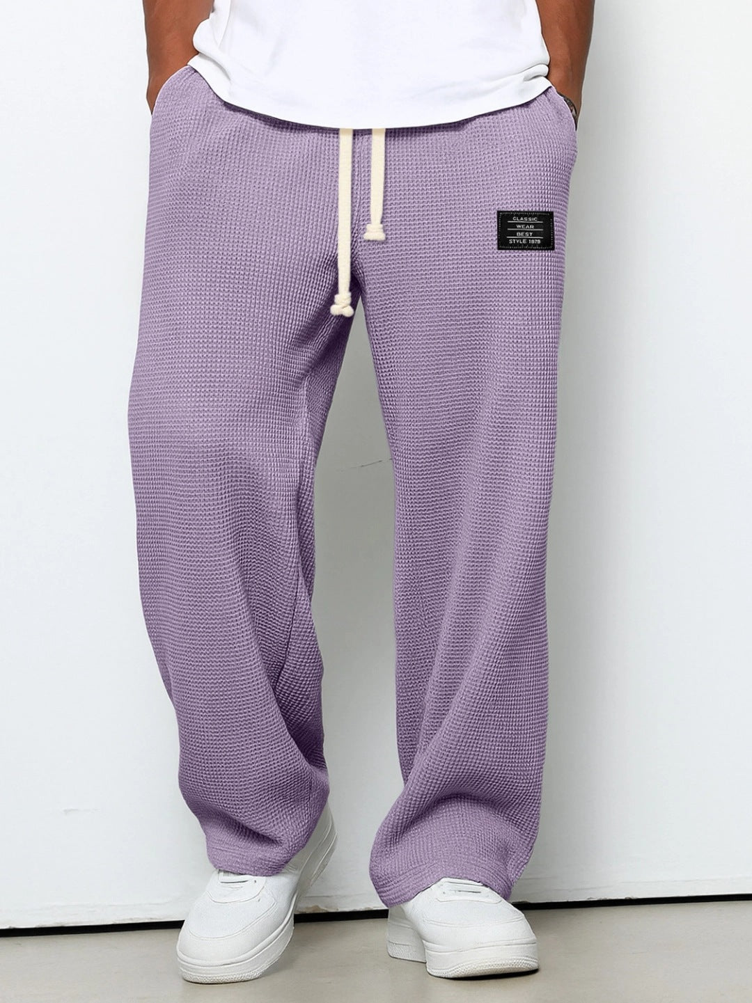 Person wearing purple textured sweatpants with a white label on a plain background