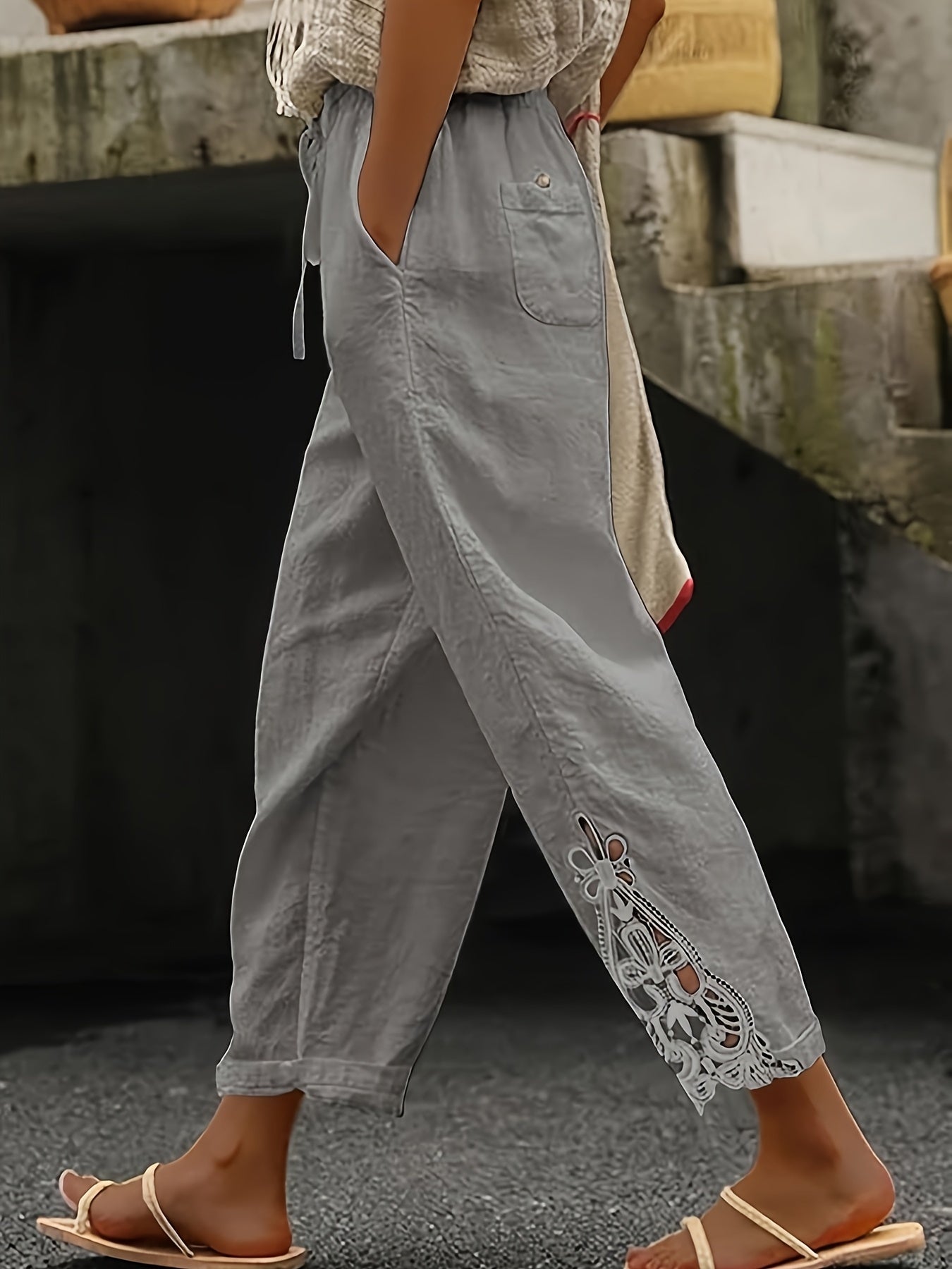 Person wearing light gray pants with lace detailing at the bottom, standing outdoors.