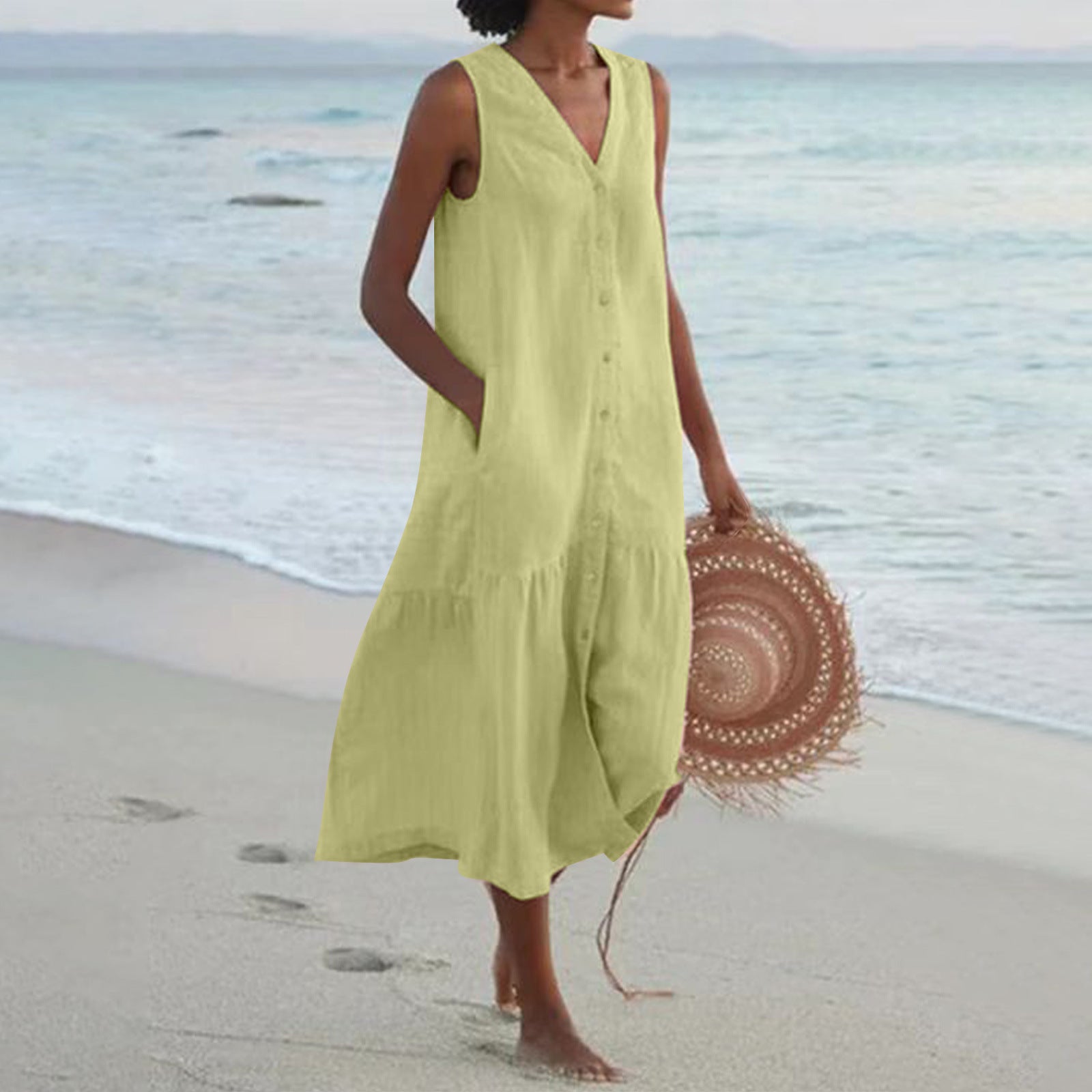 Woman in a yellow dress holding a straw hat on a beach