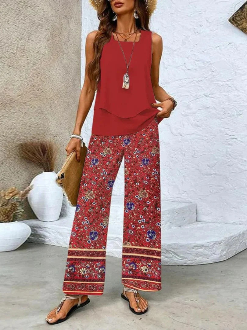 Woman wearing a red top and floral pants with a white textured wall background