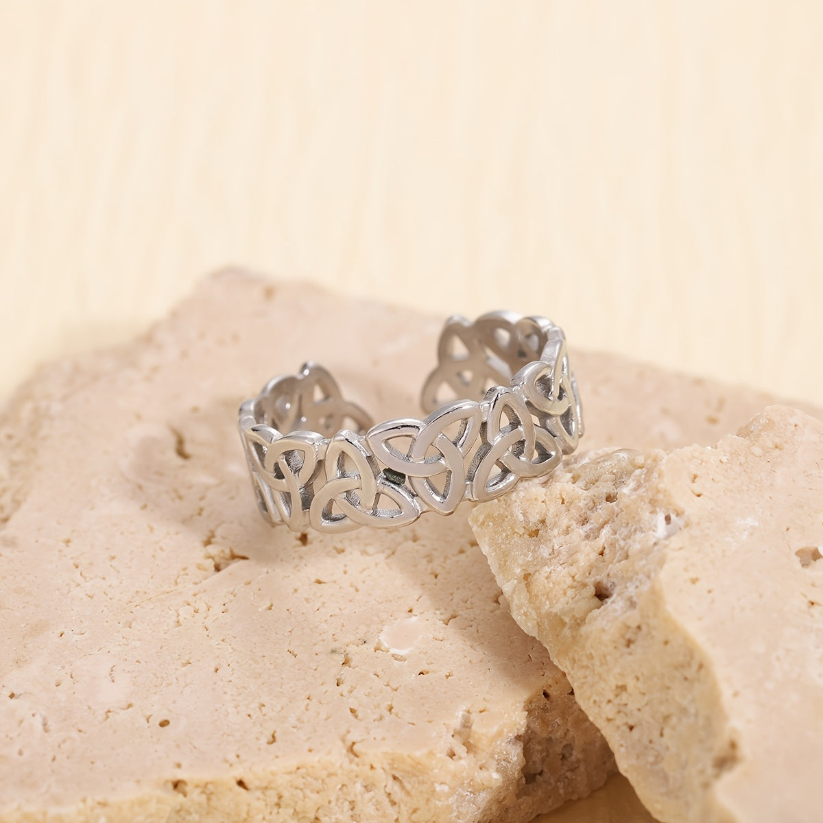 Silver ring with intricate design on a beige stone surface