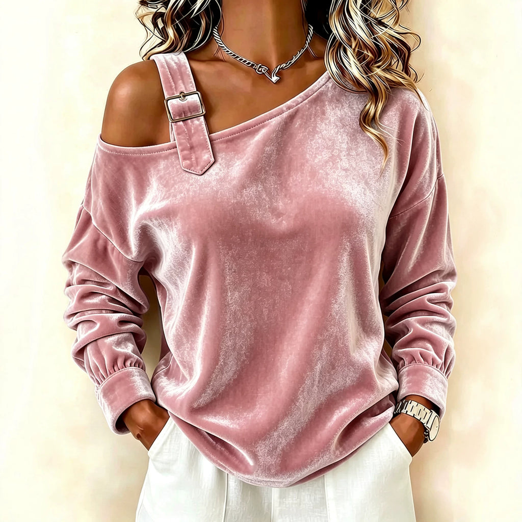 A woman wearing a dusty pink velvet off-the-shoulder long-sleeve top with a decorative strap detail and silver buckle, paired with white pants against a light beige background.
