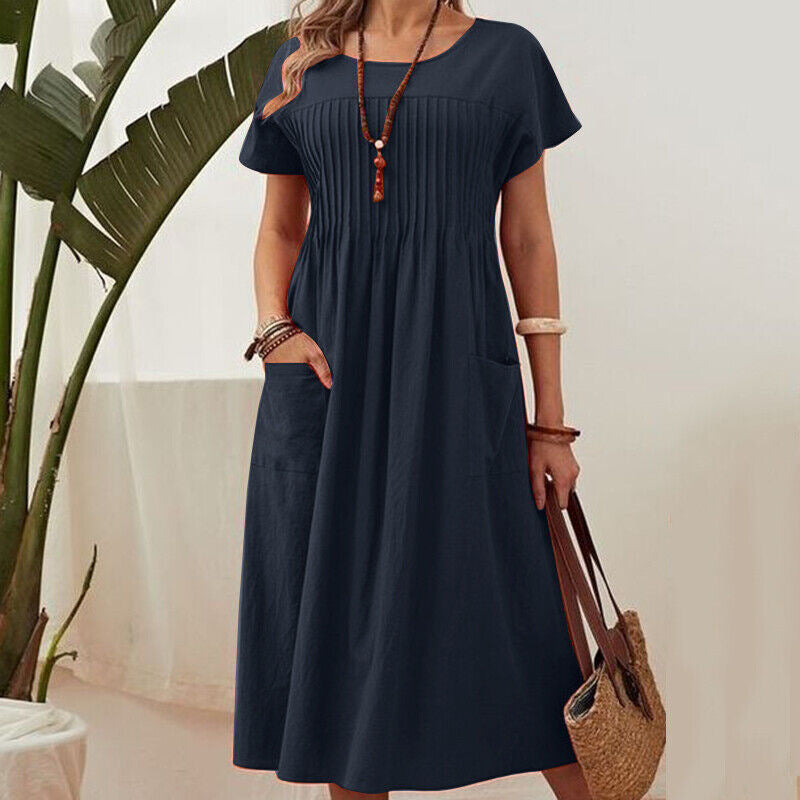 Woman wearing a navy blue dress holding a straw bag with a plant in the background