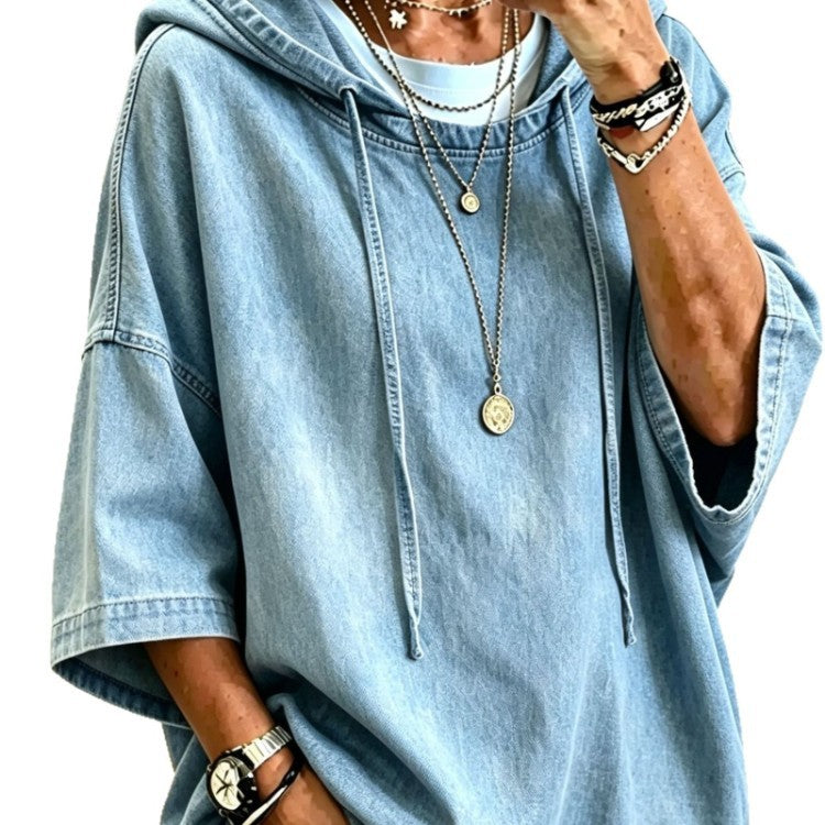A person wearing an oversized light blue denim hoodie with drawstrings, layered with multiple silver necklaces, bracelets, and a watch. The photo is cropped from the neck down against a plain white background.