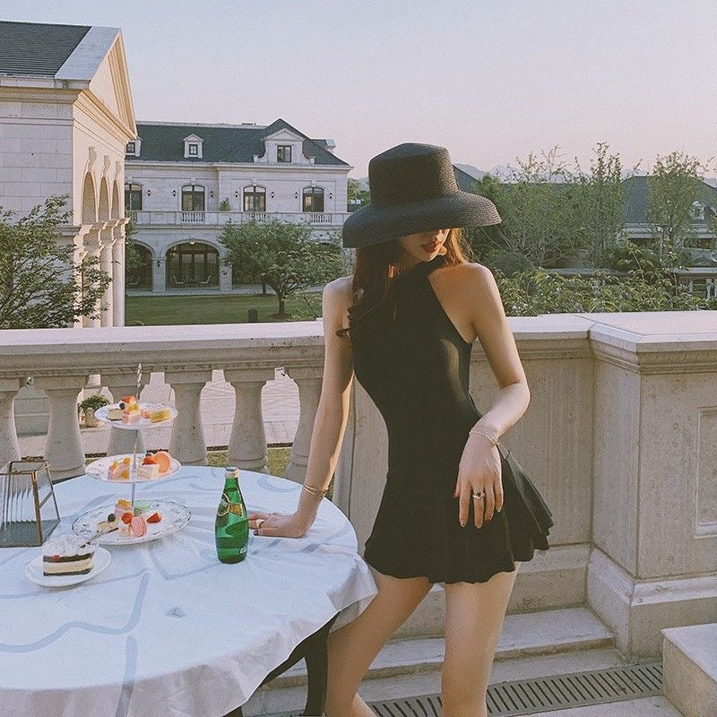 Woman in a black dress and hat standing on a balcony with a table set for a meal.