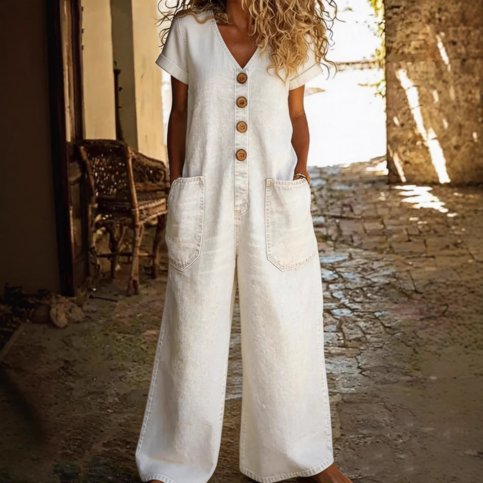 Person wearing a white denim jumpsuit with brown buttons in a sunlit outdoor setting.