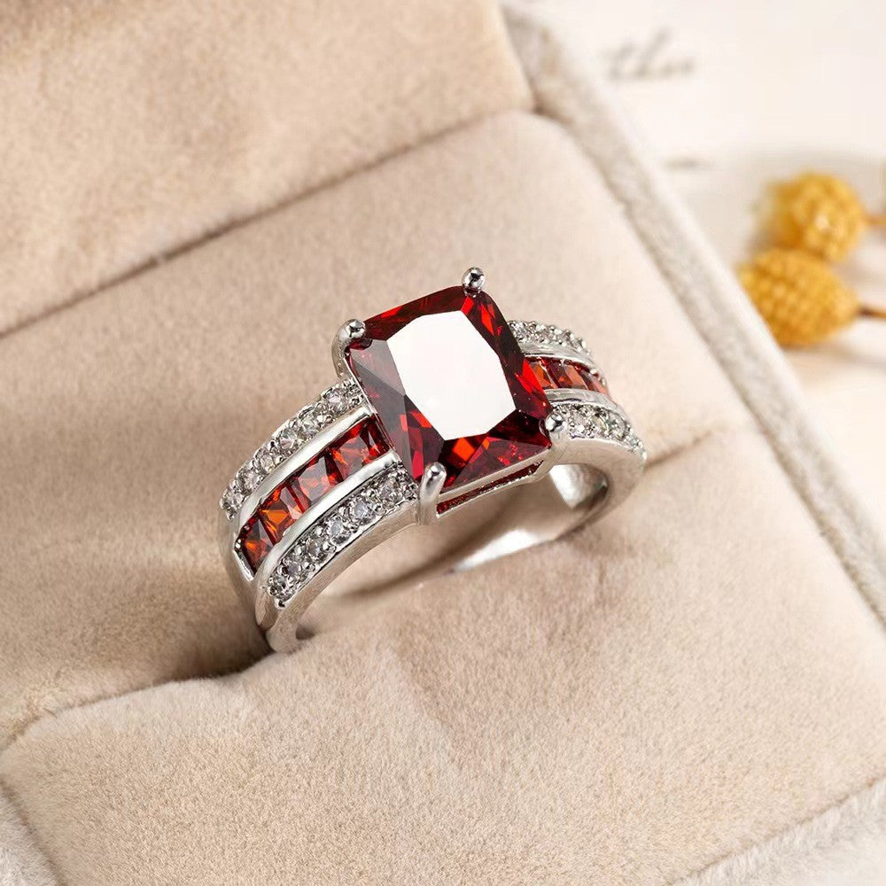 Silver ring with a large red gemstone on a beige cushion