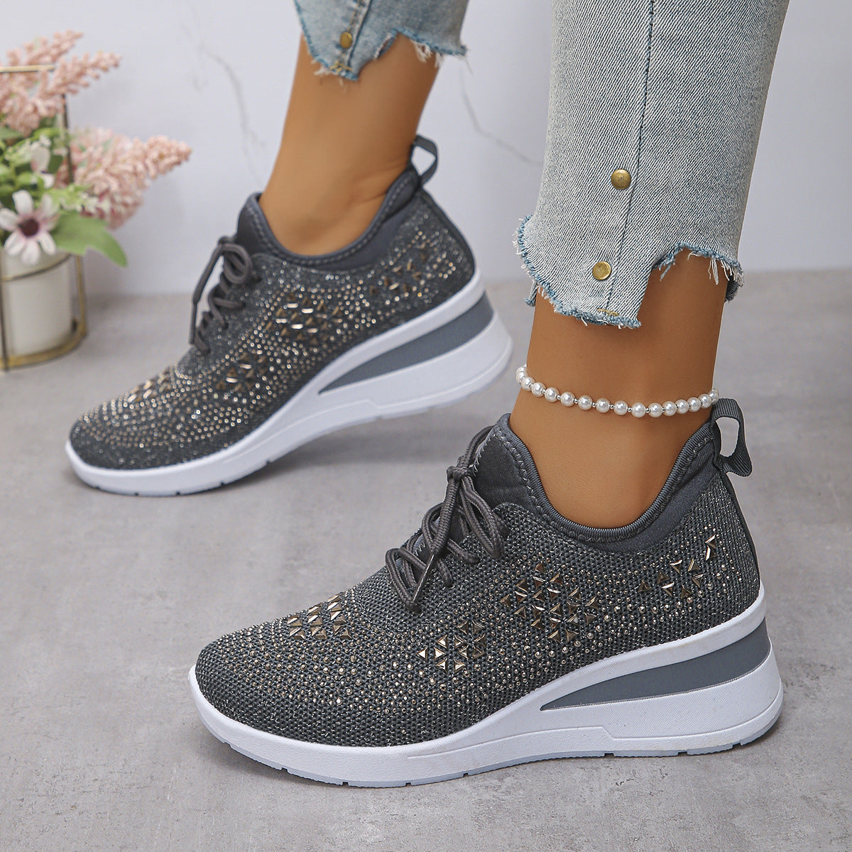 Gray sneakers with rhinestone details worn by a person on a light gray floor.