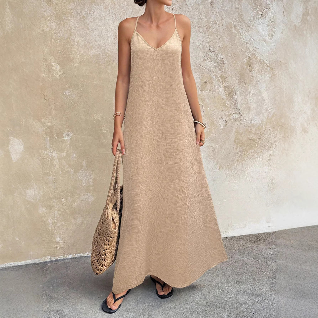 Woman wearing a beige slip dress holding a woven bag against a textured wall.