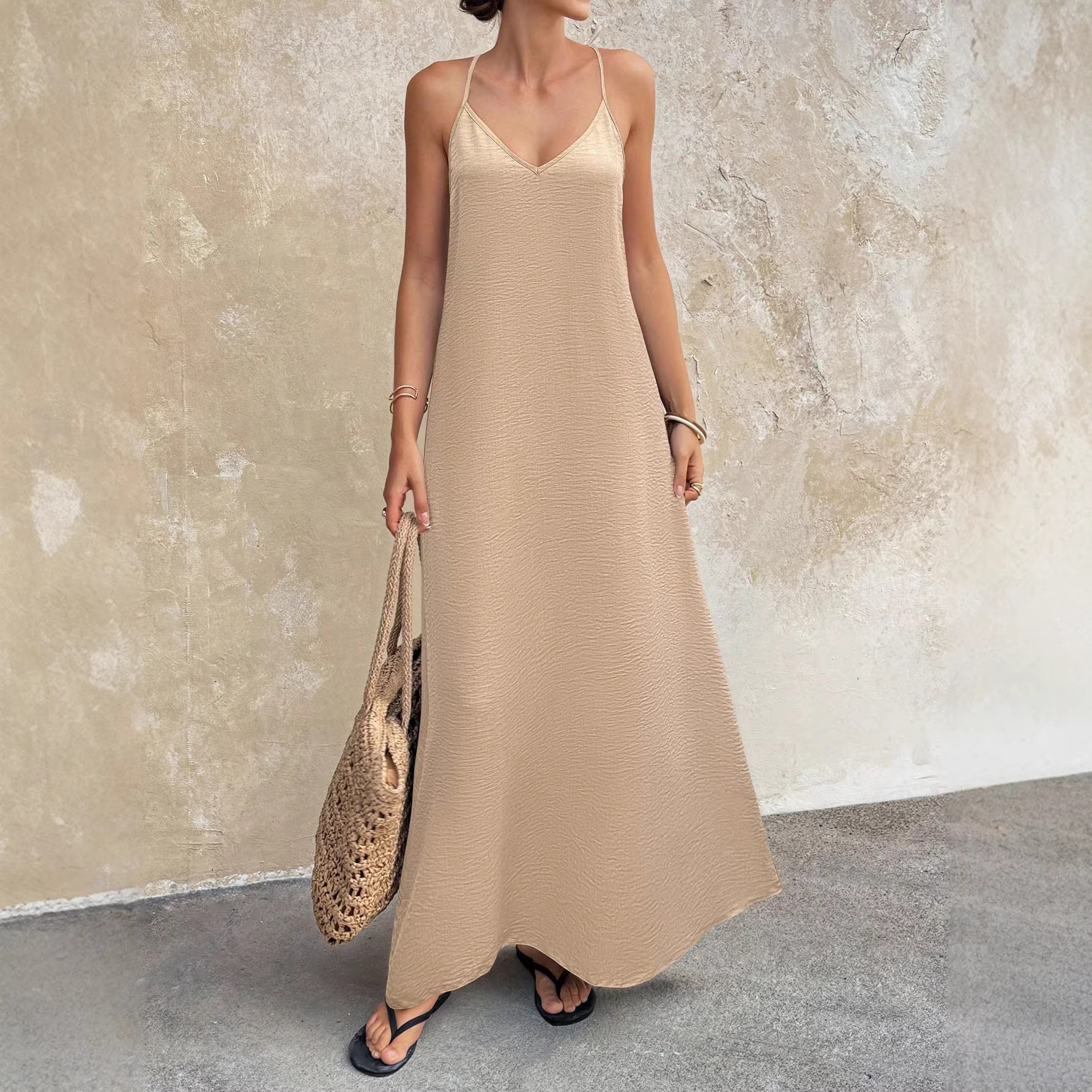 Woman wearing a beige slip dress holding a woven bag against a textured wall.