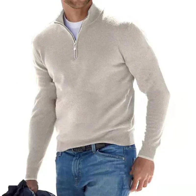 Man wearing a light gray quarter-zip sweater and blue jeans on a white background
