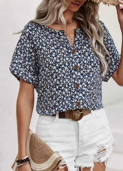 Woman wearing a blue floral blouse with white shorts against a plain background