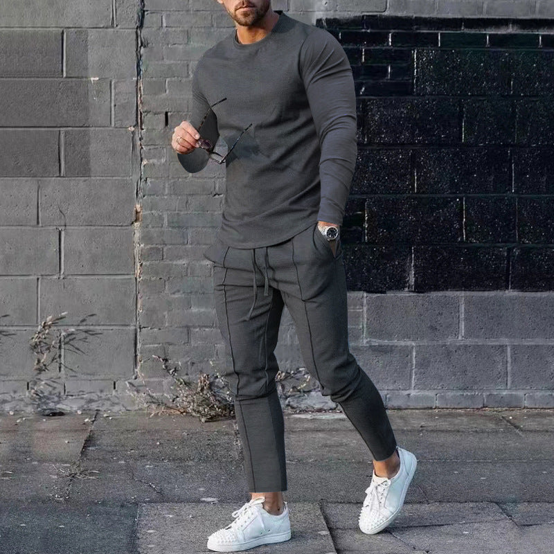 Man wearing a gray outfit with white sneakers against a brick wall.